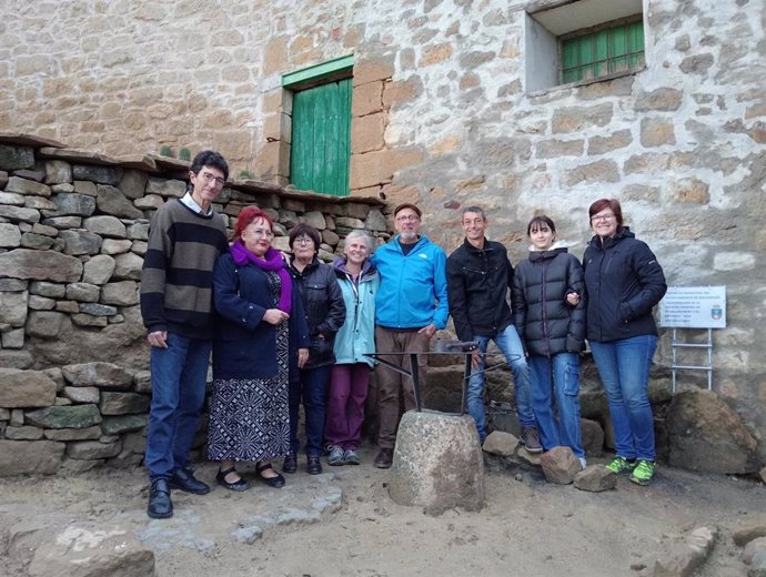 Asistentes al cierre del acto de clausura de las III Jornadas de piedra seca en Piedramorrera (Huesca) junto al molón de piedra rematado por una escultura de hierro que representa un yunque y un martillo, obra del escultor Paco Puch.