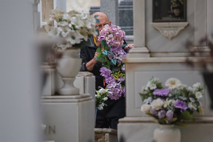 Un hombre con flores junto a una tumba en el cementerio municipal de Mérida.