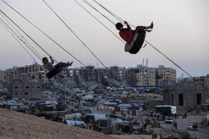 Niños palestinos juegan en un columpio entre las tiendas de campaña de los desplazados en el campamento de Khan Yunis, en el sur de la Franja de Gaza