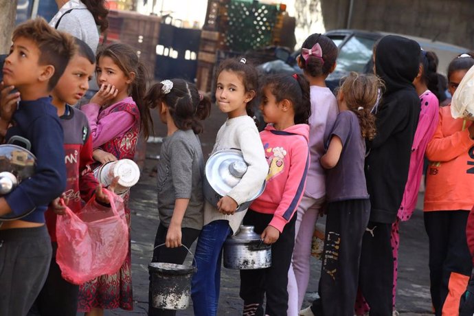 Niños palestinos desplazados hacen cola para recibir raciones de comida ofrecidas por una organización benéfica