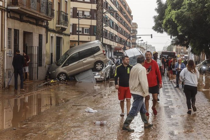 Varias personas recorren calles llenas de agua y barro tras el paso de la DANA por el barrio de La Torre