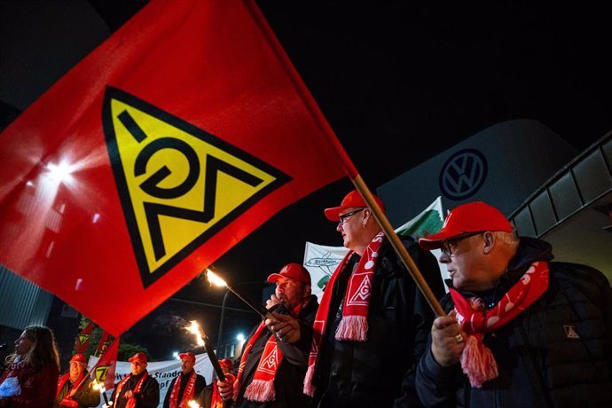 29 October 2024, Osnabrueck: Volkswagen employees stand with torches and flags as they take part in a warning strike in front of the VW plant in Osnabrueck. 