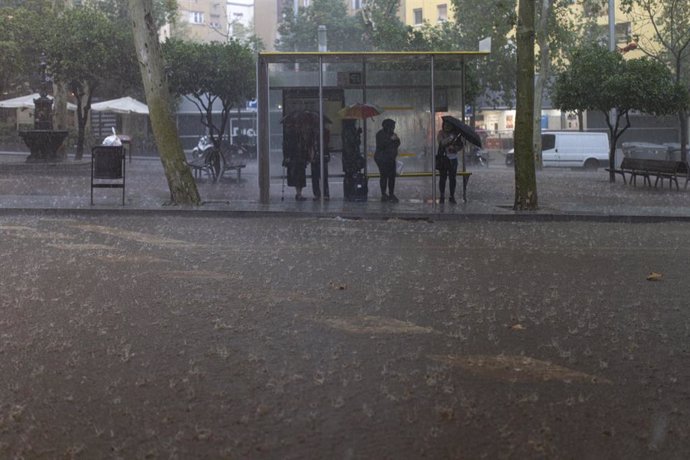 Varias personas esperan en la parada del bus durante la tormenta en Barcelona.