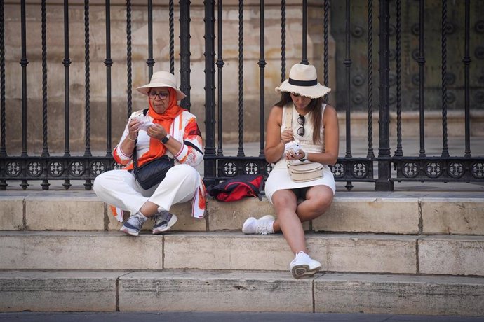 Archivo - Dos turistas sentadas en los escalones de la Catedral de Sevilla.