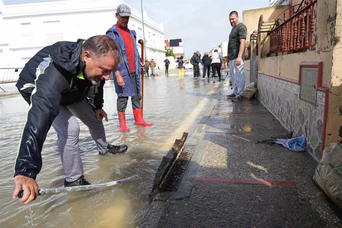 Varios vecinos de la calle Buen Pastor, de San Fernando, intentan desatascar una alcantarilla ,a 31 de octubre de 2024, en Cádiz (Andalucía, España).