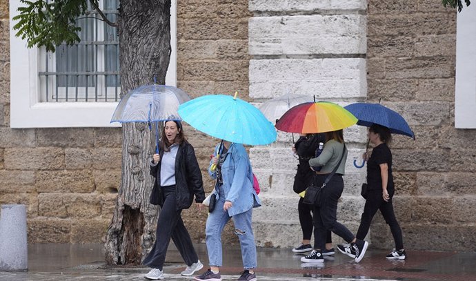 Varias personas con paraguas se refugian de la lluvia.