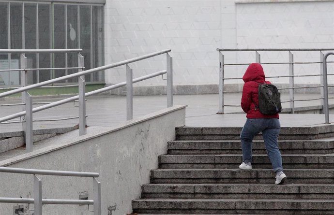 Archivo - Una mujer sube unas escaleras y se protege del viento con el abrigo a 14 de noviembre de 2019.