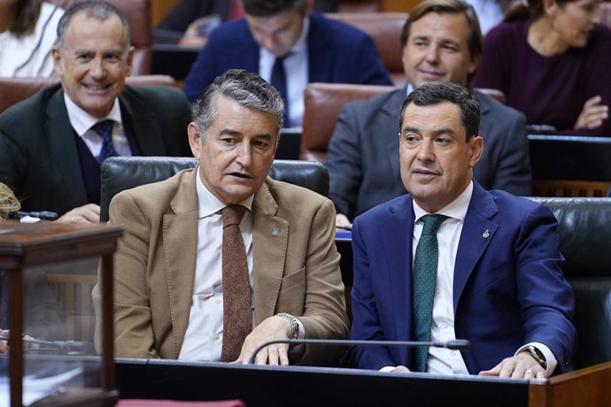 El presidente de la Junta de Andalucía, Juanma Moreno (d) conversa con el consejero de Presidencia, Antonio Sanz (I), en el Pleno del Parlamento. (Foto de archivo).