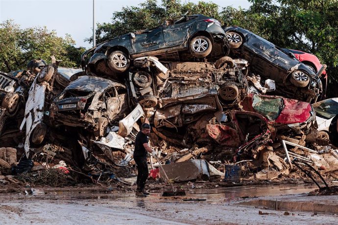 Varias personas limpian entre coches amontonados en Alfafar tras el paso de la DANA