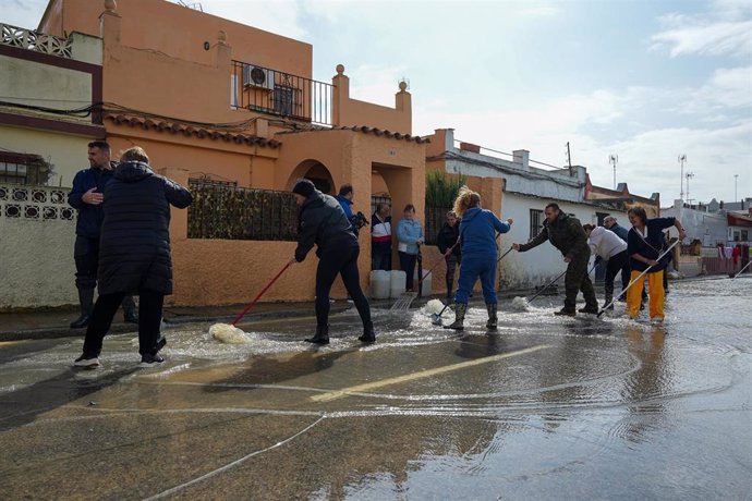 Varios vecinos de la calle Buen Pastor, en el municipio de San Fernando (Cádiz), barren el agua a la alcantarilla tras las lluvias caídas en la mañana del 31 de octubre de 2024. 