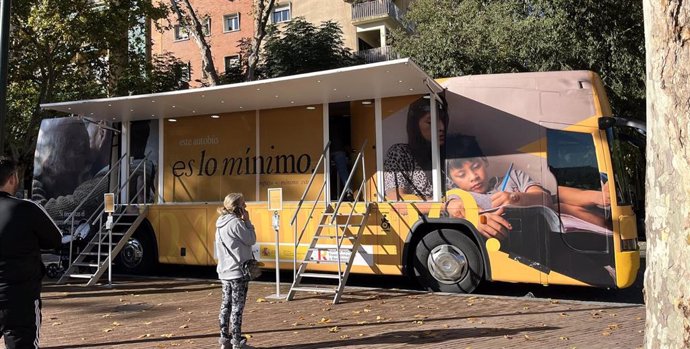 Archivo - Una mujer habla por teléfono delante del autobús del Ingreso Mínimo Vital