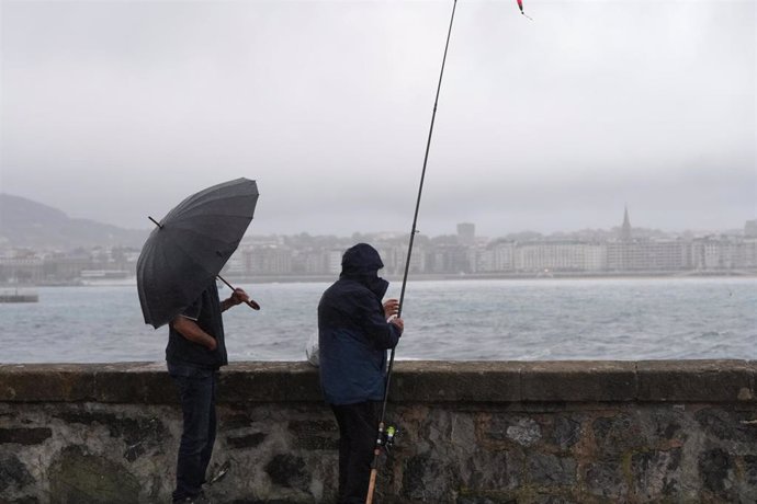 Archivo - Dos personas bajo la lluvia en la playa de Ondarreta