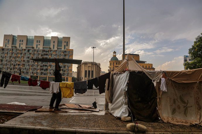 November 2, 2024, Beirut, Beirut, Lebanon: A man, who fled with his family Beirut southern suburb to take refuge in an open area in Beirut downtown, holds a card board as he prepares to fortify and protect his tent from pouring rain. Distraught families, 