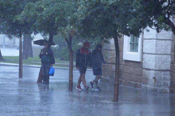 Archivo - Transeuntes bajo sus paraguas durante la intensa lluvia en Cádiz.