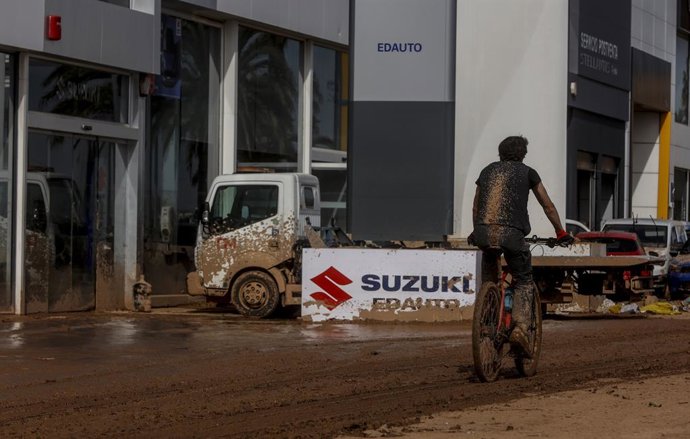 Un home passa amb una bicicleta al costat d'un concessionari del polígon Alcedo després del pas de la DANA, a 8 de novembre del 2024, a Valncia.