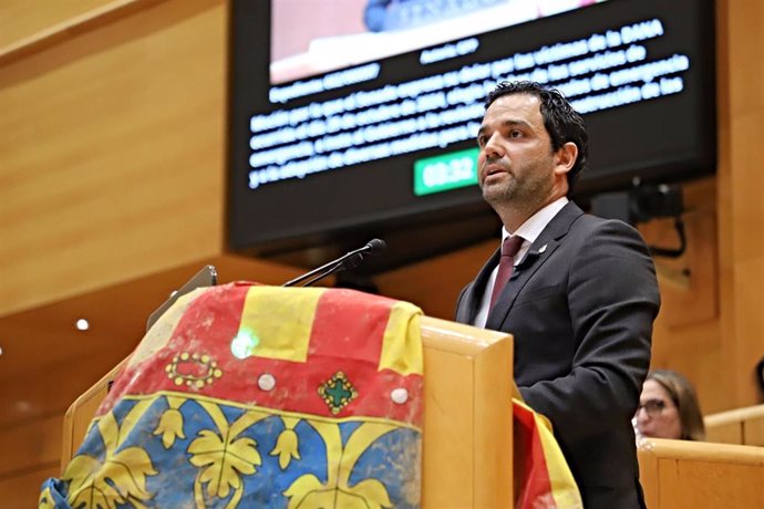 El senador del PSOE y alcalde de Paterna (Valencia), Juan Antonio Sagredo, despliega en el Senado una bandera de la Comunidad Valenciana manchada por el barro de la DANA.