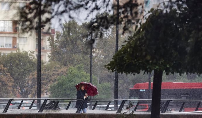 Archivo - Una mujer camina mientras se protege de la lluvia con un paraguas