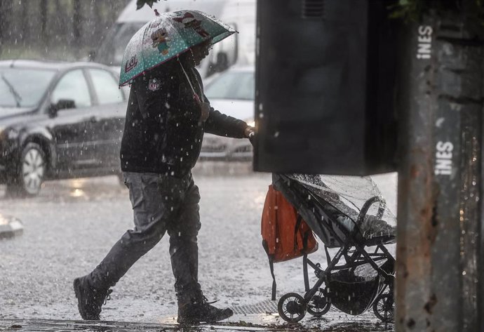 Archivo - Un hombre lleva un carrito de bebé mientras se protege de la lluvia con un paraguas