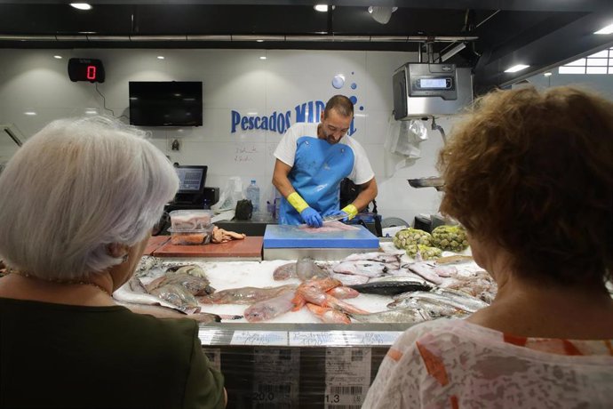 Archivo - Varias personas compran alimentos en un mercado.