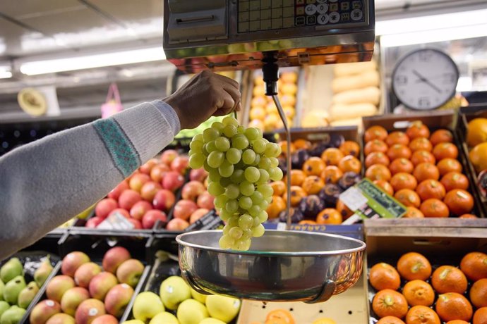 Archivo - Imagen de archivo de un dependiente pesa un racimo de uvas en un mercado.