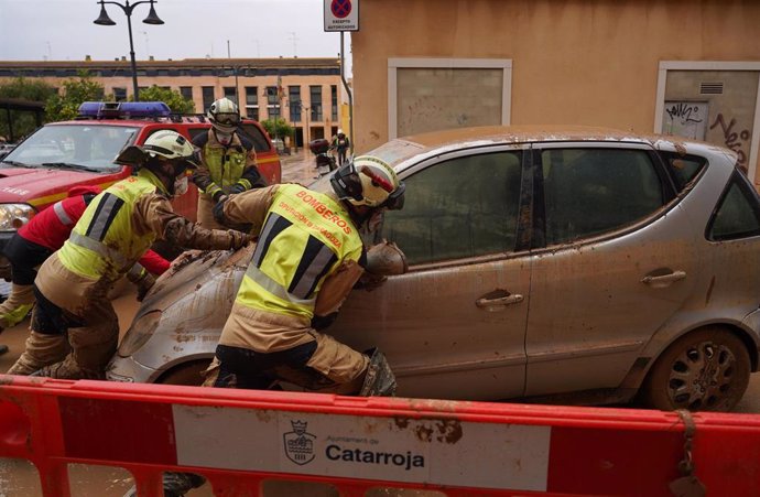 Dos personas ayudan a retirar un coche dañado por la DANA en Catarroja