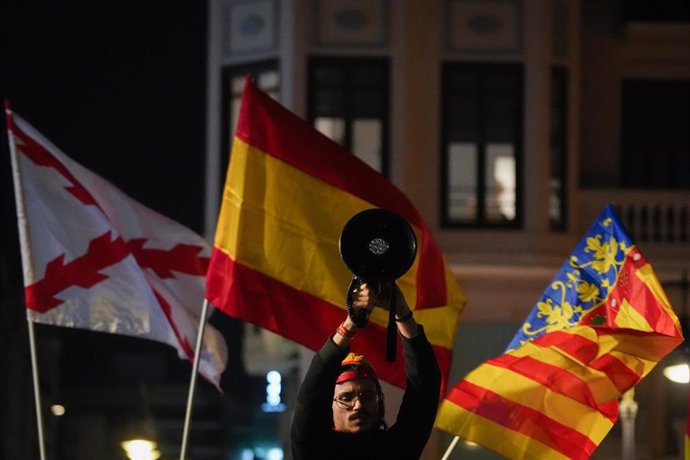 Una persona sostiene un altavoz rodeado de banderas, durante la manifestación contra Sánchez y Mazón, en la Plaza de San Agustín de València, convocada por Revuelta