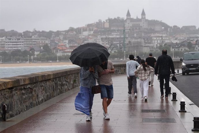 Archivo - Dos personas se protegen de la lluvia con un paraguas en la playa de Ondarreta