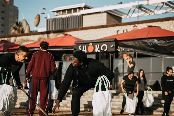 Jóvenes voluntarios y trabajadores del Front Marítim recogen basura en la playa del Somorrostro de Barcelona en una jornada organizada por la discoteca Shôko con la colaboración de la ONG PlasticFREEWave