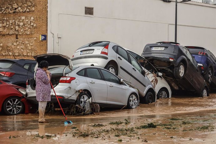 Una mujer realiza labores de limpieza junto a vehículos destrozados tras el paso de la DANA por el barrio de La Torre de Valencia, a 30 de octubre de 2024, en Valencia, Comunidad Valenciana (España).