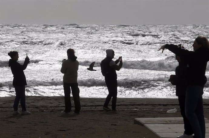 Archivo - Varias personas en la playa de la Malagueta donde el temporal azota con fuertes vientos y oleaje. Imagen de archivo. 