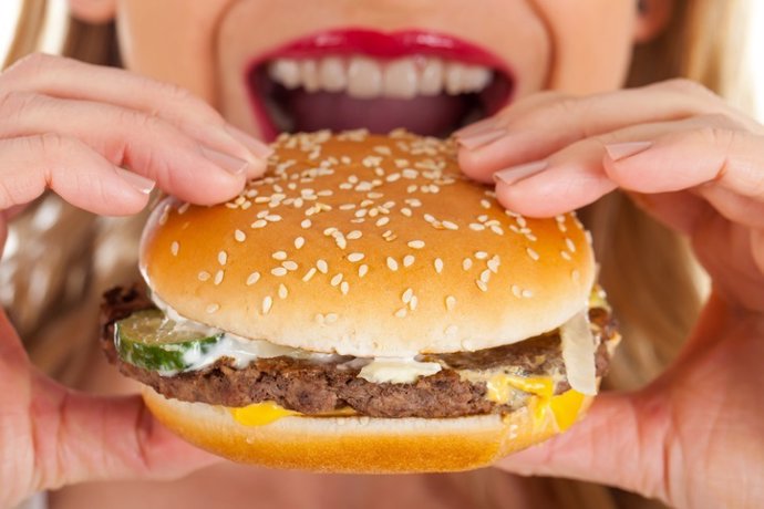 Archivo - Una mujer comiendo una hamburguesa