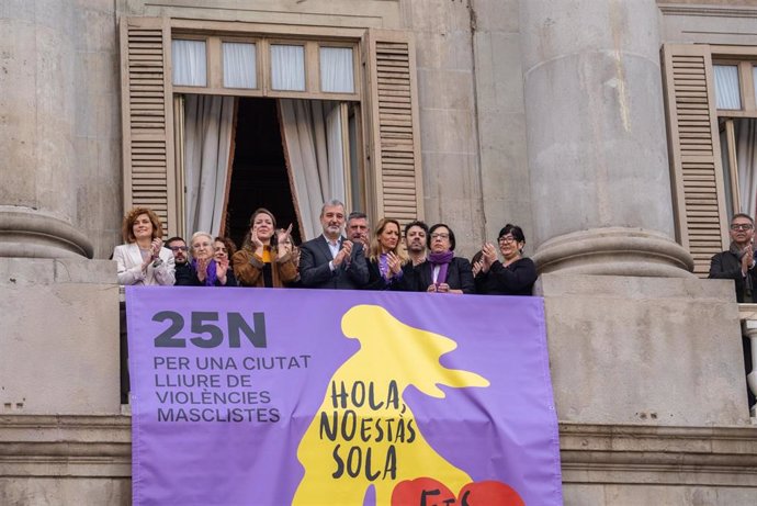 El alcalde Jaume Collboni junto a miembros de los grupos municipales colgando la pancarta del 25N en el balcón del consistorio