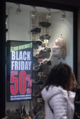 Archivo - Una persona pasa por delante de una tienda que anuncia un cartel publicitario del Black Friday