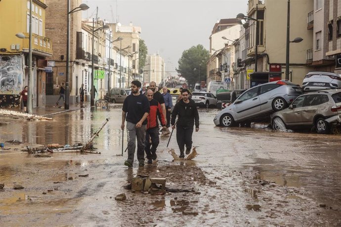 Imgaen de archivo de varias personas que recorren calles llenas de agua y barro tras el paso de la DANA.