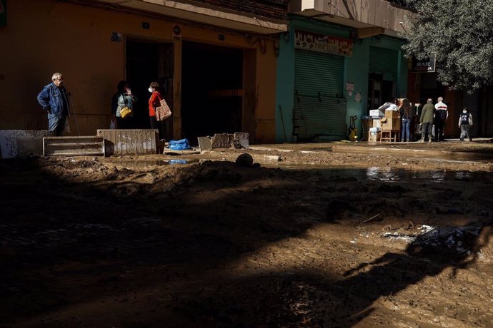 Diverses persones en un carrer cobert de fang, a 28 de novembre del 2024, a Paiporta, un mes després de la dana.