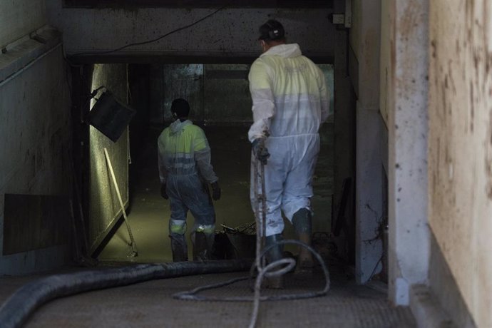 Dos trabajadores durante la presentación de los nuevos dispositivos para la extracción de lodo en garajes y plantas bajas, en la Plaça País Valencià, a 27 de noviembre de 2024