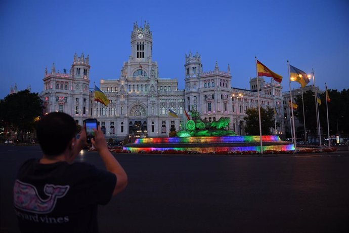 Archivo - Una persona fotografía la fuente y el Palacio de Cibeles con los colores de la bandera LGTB