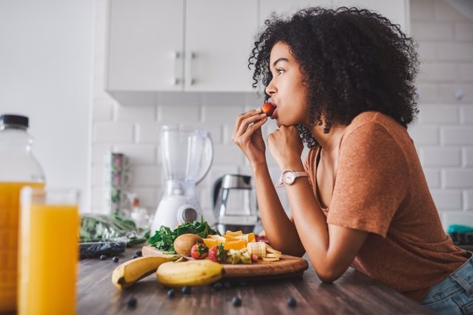 Archivo - Mujer comiendo fruta en la cocina.