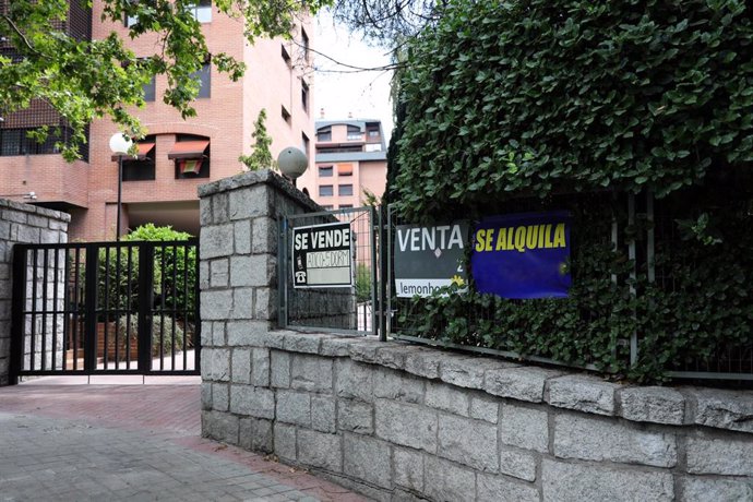 Archivo - En la valla de una urbanización, se ven colgados dos carteles de 'Se vende piso' y uno de 'Se alquila'.