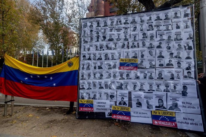 Un cartel de protesta con fotografías junto a una bandera de Venezuela durante una manifestación de venezolanos en Madrid