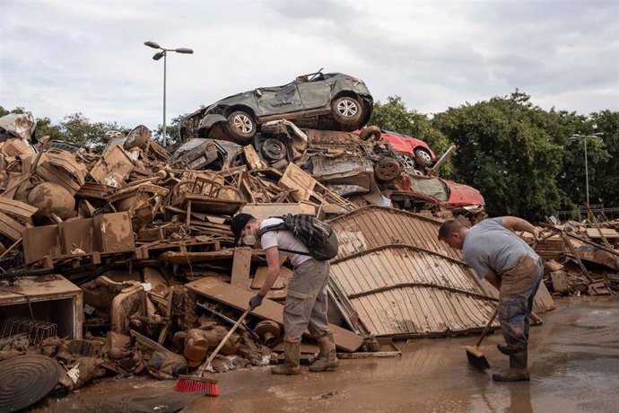 Dos personas realizan labores de limpieza al lado de una montaña de basura, vehículos y mobiliario destrozado tras el paso de la DANA 