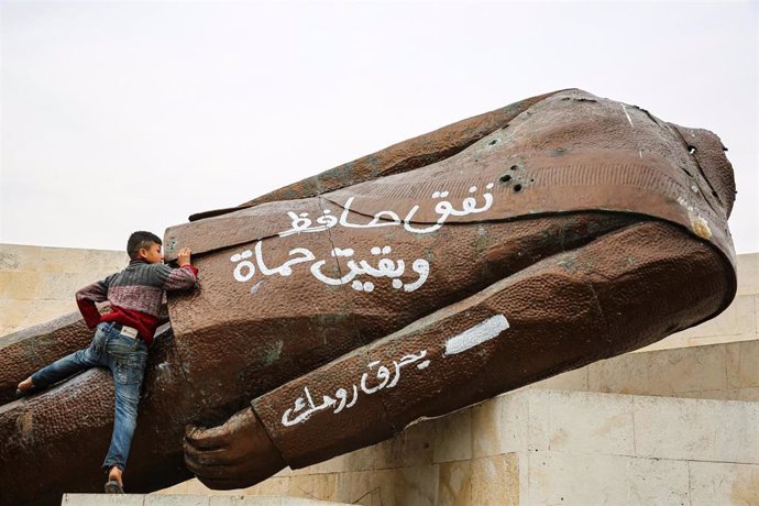 Un niño escala sobre una estatua derribada de Hafez al Assad en Hama (Siria)