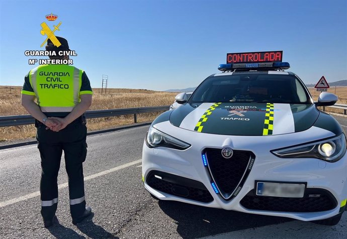 Archivo - Imagen de archivo de un agente de la Guardia Civil de Tráfico junto a su vehículo en una carretera.