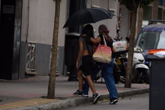 Archivo - Dos mujeres se protegen de la lluvia con un paraguas