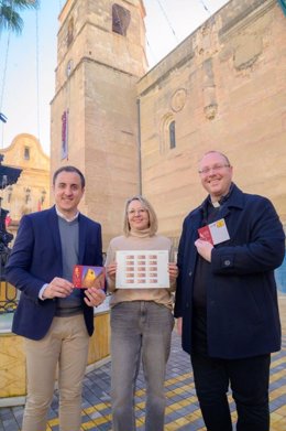 El alcalde de Vera (Almería), Alfonso García, exhibe los productos filatélicos con la imagen de la Iglesia de la Encarnación junto al párroco y la responsable de la oficina de Correos de Vera.