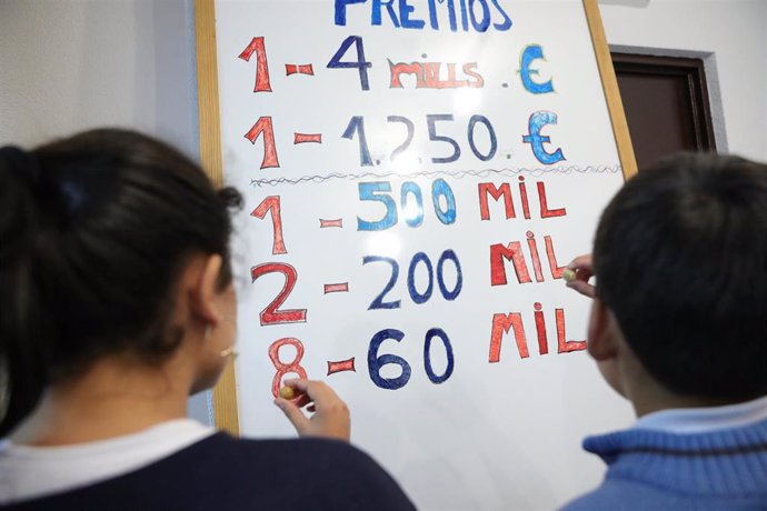 Archivo - Dos niños de la Residencia Internado San Ildefonso apuntan en una pizarra el número de premios y la cantidad correspondiente a cada uno, preparándose para la celebración del Sorteo de la Lotería de Navidad del próximo 22 de diciembre, en Madrid 