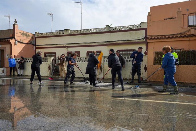 Archivo - Varios vecinos de la calle Buen Pastor, de San Fernando, barren el agua a la alcantarilla el 31 de octubre.