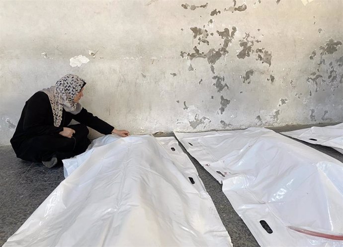 Una mujer junto a los cadáveres de dos palestinos muertos en ataques del Ejército de Israel tras ser trasladados al Hospital Baptista Al Ahli de la ciudad de Gaza, en el norte de la Franja de Gaza