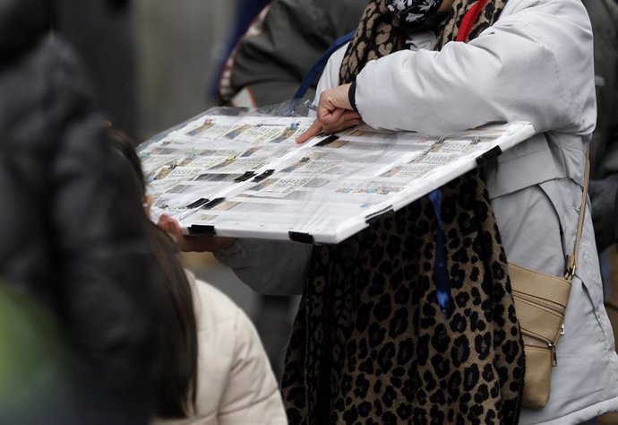 Archivo - Una personas compra un décimo de lotería de Navidad a una vendedora ambulante