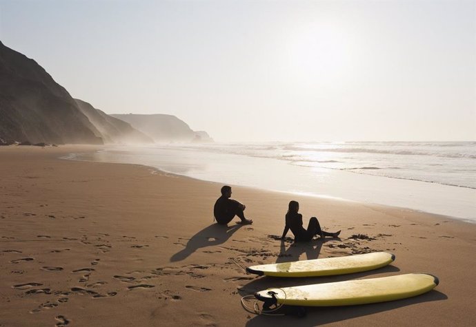 Pareja de turistas descansando en una playa junto a unas tablas de surf